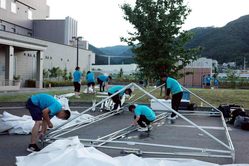 屋外でテントの骨組みを組み立てるスタッフ